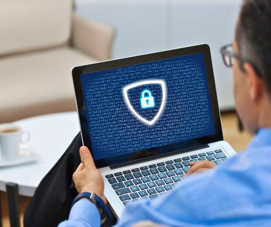 Person using a laptop displaying a glowing shield with a padlock, symbolizing cybersecurity.